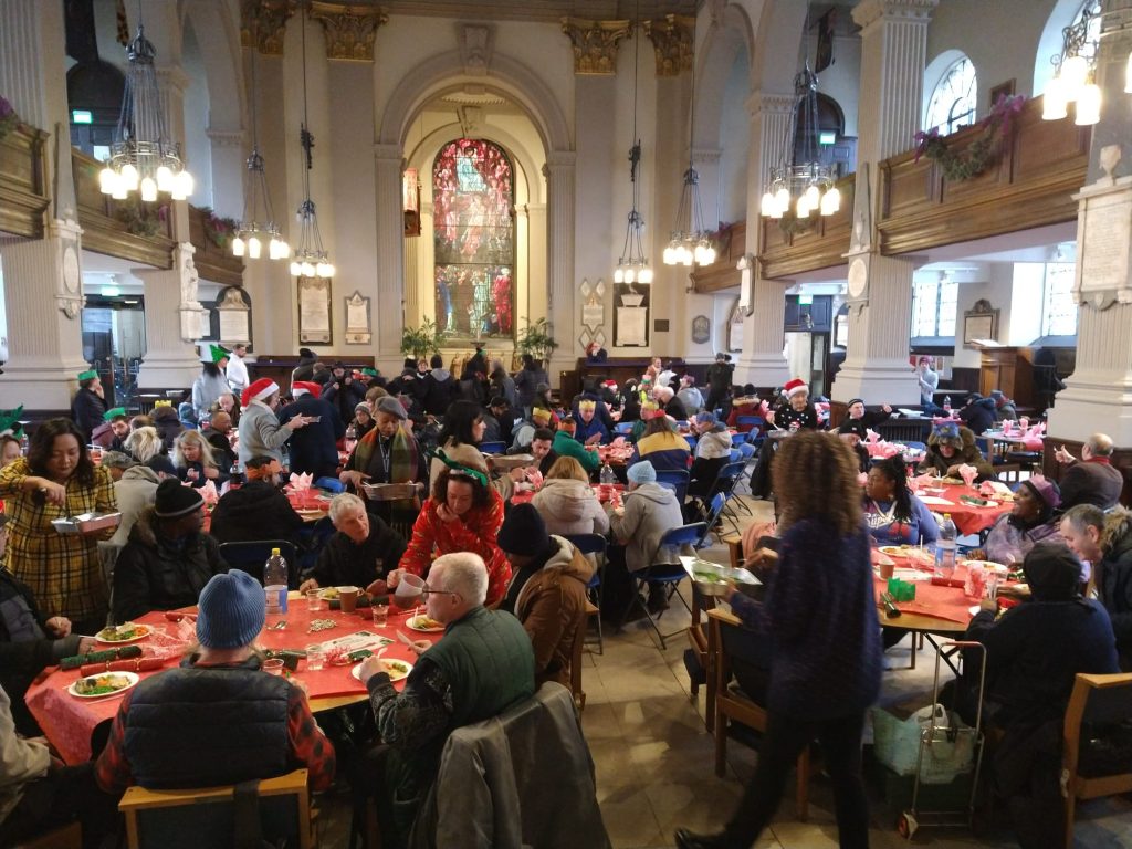 St Philips Cathedral Birmingham filled with festively decorated round tables laden down with Christmas feast being enjoyed by the people that Let's Feed Brum supports.
